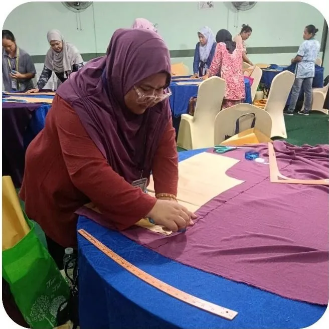 Peserta kursus menjalankan kerja memotong kain di atas meja potong